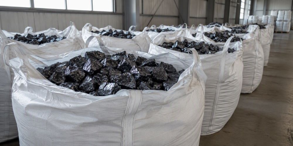 Open woven bulk bags filled with silicon metal lumps lined up on a warehouse floor.