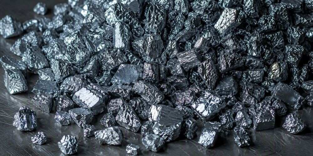 A heap of shiny pea-sized metallic silicon granules on dark steel.