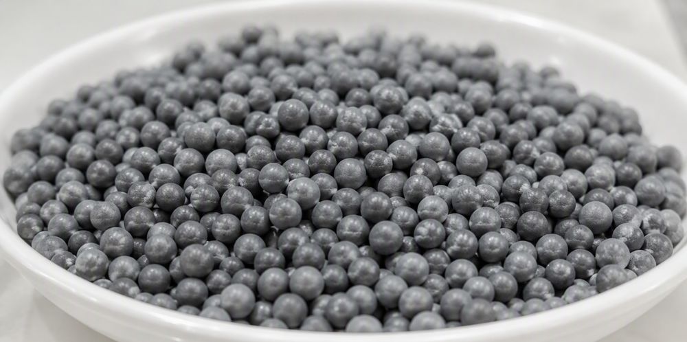 Near-spherical gray polysilicon beads filling a shallow white ceramic dish.