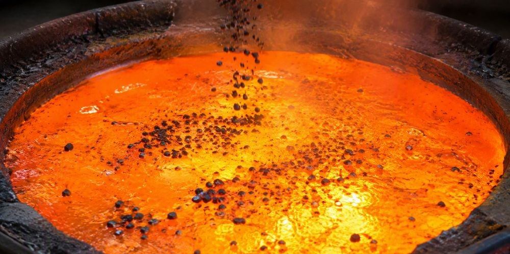 Dark silicon granules sinking into the glowing surface of molten aluminum in a ladle.