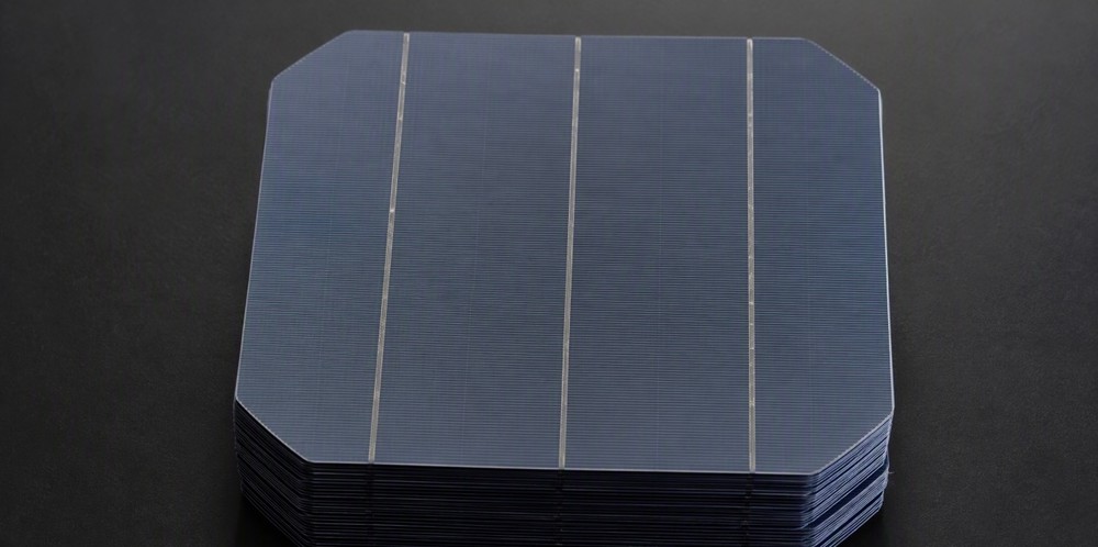 A top-down view of a tidy stack of dark pseudo-square solar wafers with chamfered corners.