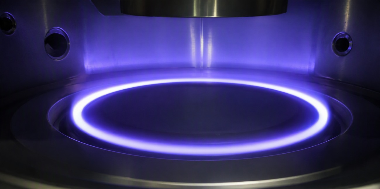 A bright ring of plasma racing over a circular silicon target inside a sputtering chamber.