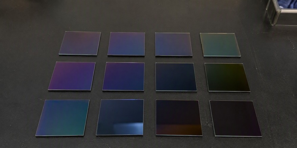 Small square thin-film silicon coated coupons arranged in a grid on a dark bench.