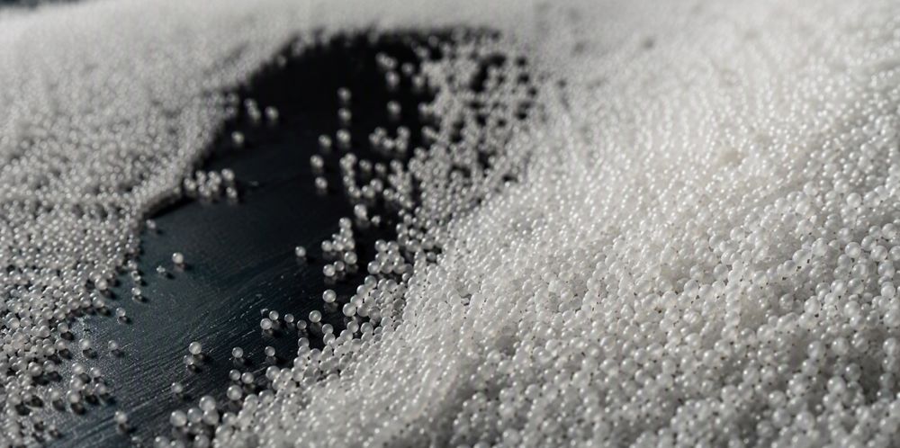 Countless tiny white spherical silica microspheres flowing across a dark surface.