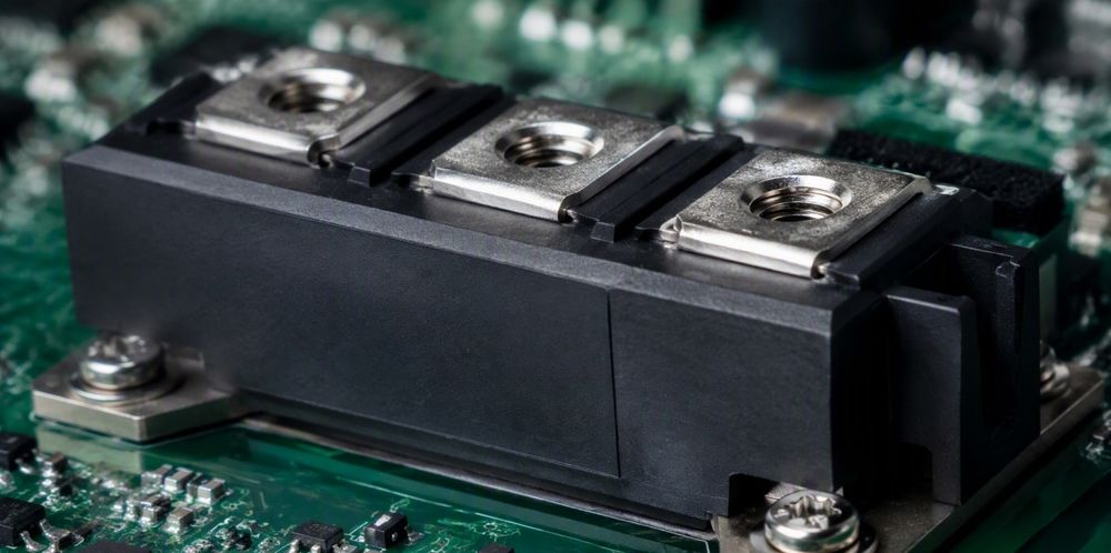 A black power semiconductor module with silver terminals on a green circuit board.