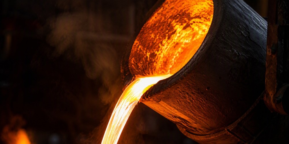 A dark ceramic crucible tilting a bright stream of molten aluminum.