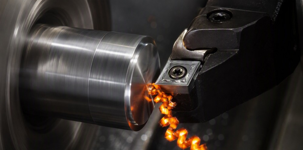 A cutting tool shaping spinning metal with glowing orange chips.