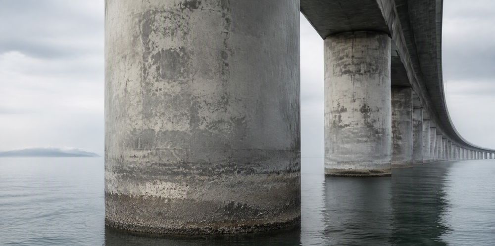 Weathered concrete bridge columns standing in calm coastal seawater.