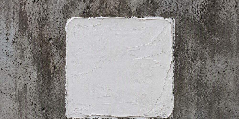 A square patch of white silane cream applied to a gray concrete wall.