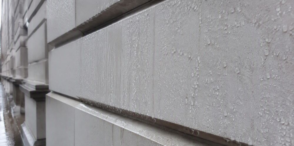 Rainwater beading and running down a light stone building facade.