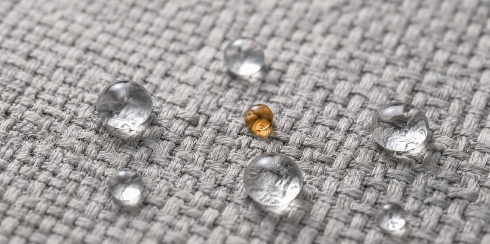 Round water and oil droplets resting on a woven fabric surface.