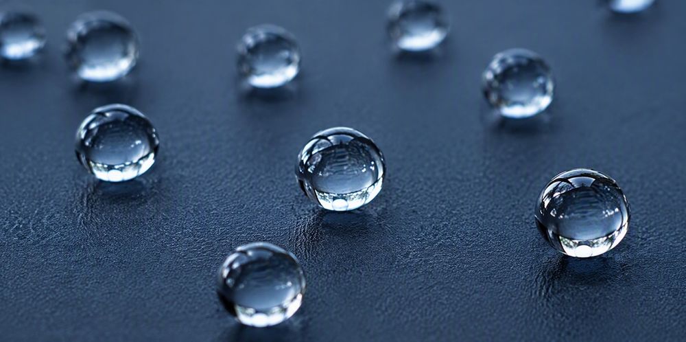 Round water droplets beading on a dark water-repellent surface.