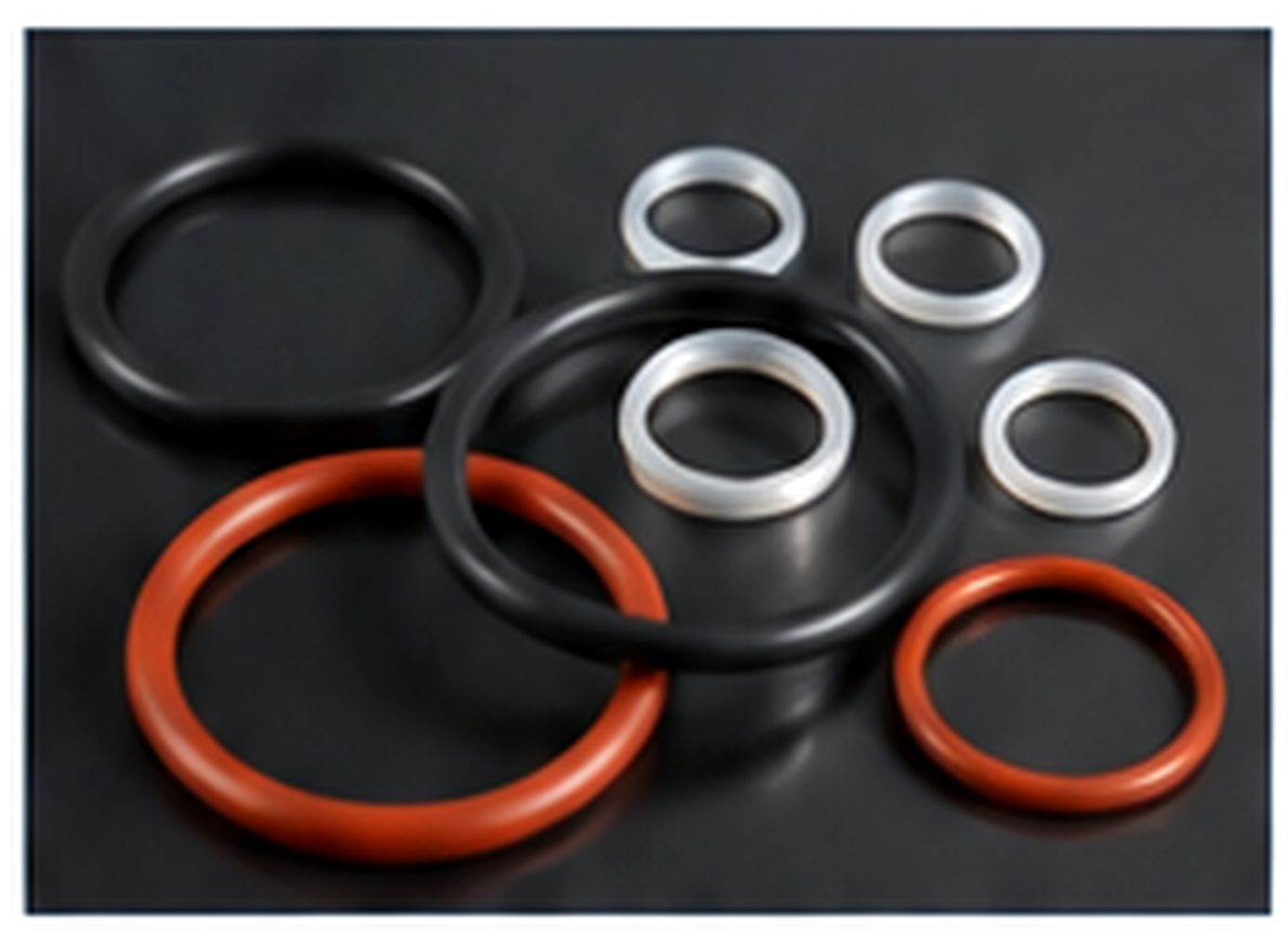 Assorted black, white and orange silicone O-rings grouped on a dark surface.