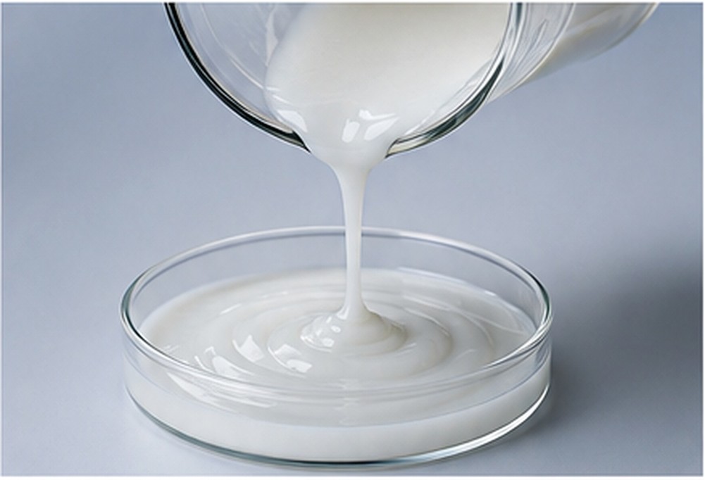 Opaque white slurry pouring smoothly into a glass dish as a dispersion-processing example.